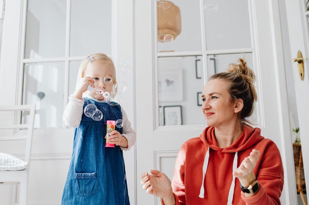 A joyful moment of a mother and daughter playing with bubbles indoors.